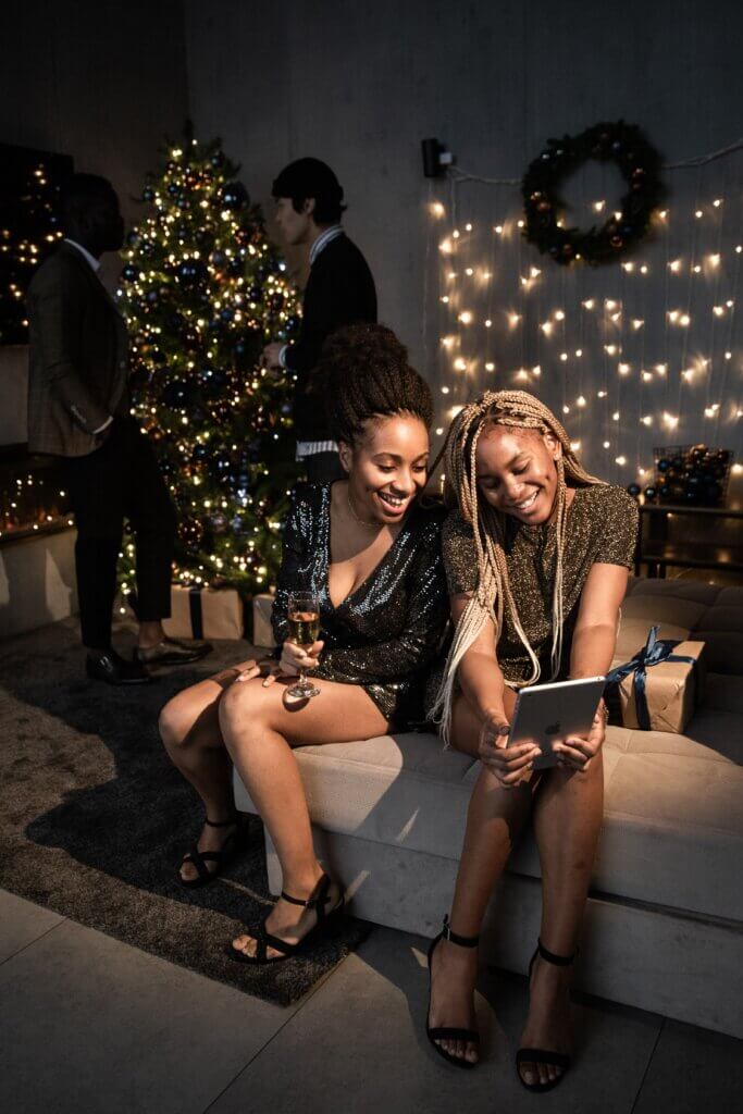 Two women sitting by a Christmas tree at a holiday party
