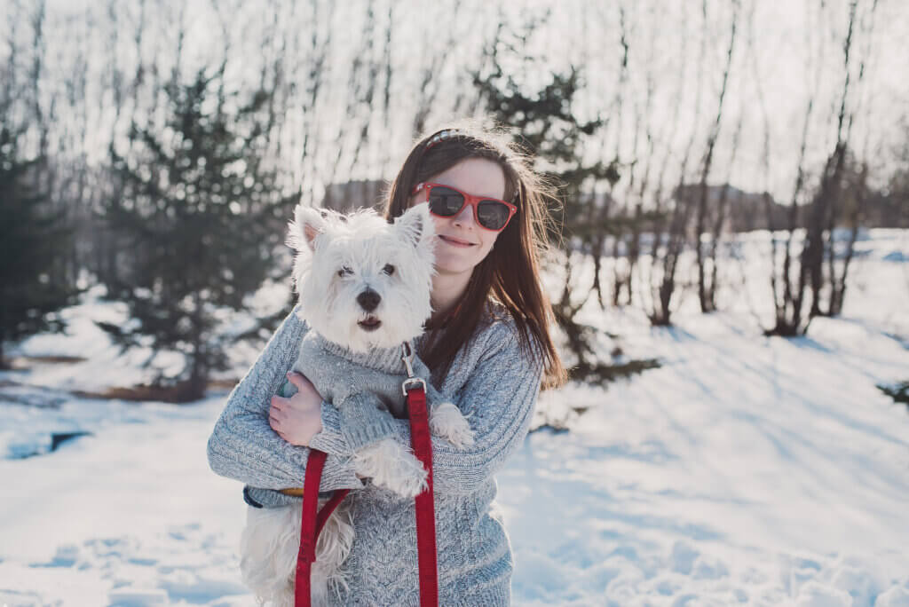 A woman holding a westie dog outside in the winter