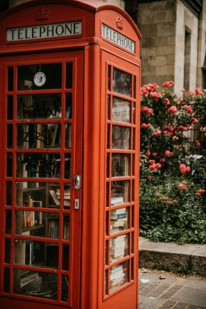Red phone booth library in London with flowers in the background